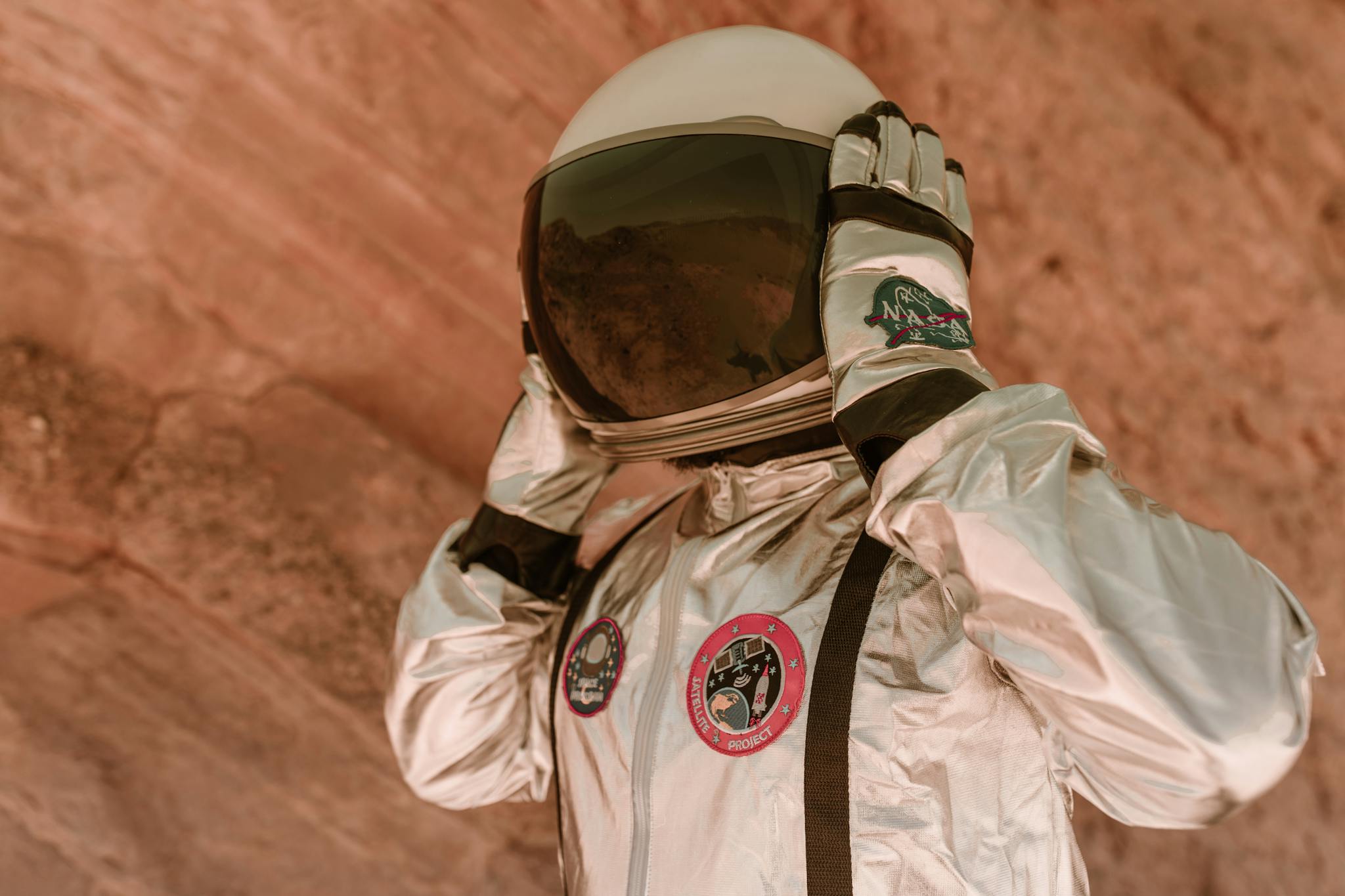 Close-up of astronaut wearing a silver spacesuit in a rocky outdoor environment.
